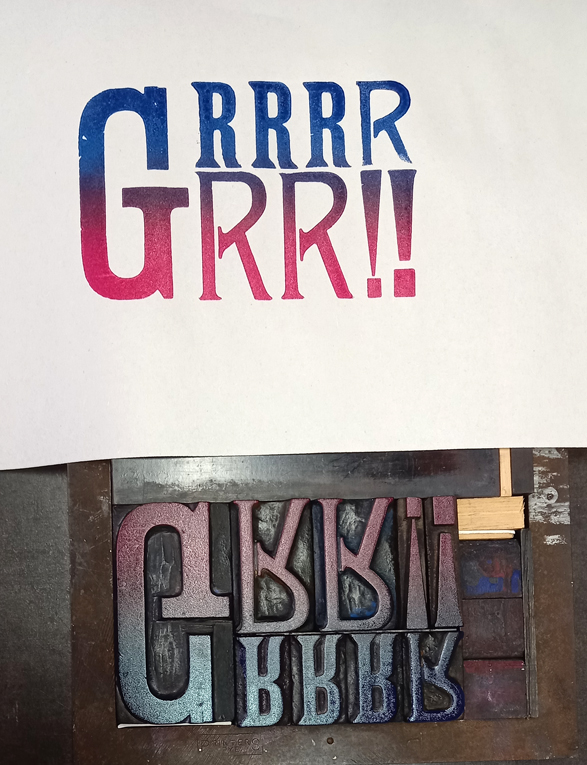 A typeface form showing the word Grrr in reverse in different sized vintage wooden typefaces has been inked with blue and red, and the print of it is shown on white paper.