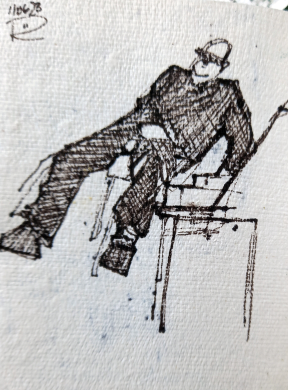 A small line drawing of a man in black shirt, trousers and boots leaning back in an armless chair. He looks very comfortable, both his feet are off the floor. He wears glasses and his right hand rests on his left thigh while his left hand rests on a table and supports himself and the tilted chair